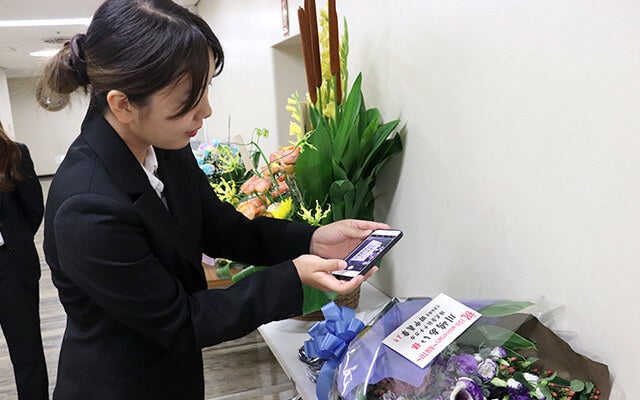 控室前の花束の写真を撮る田中さん2