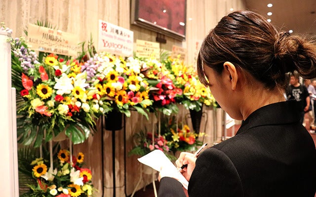 ロビーに飾られている贈花のメモをとる田中さん