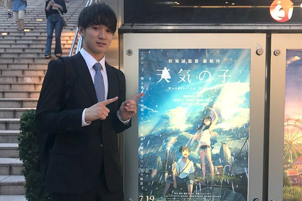 外のポスターの前で記念撮影する高野さん