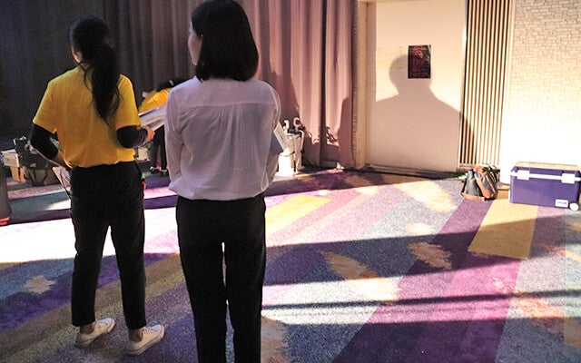 舞台裏で司会の二人を見守る高村さん写真