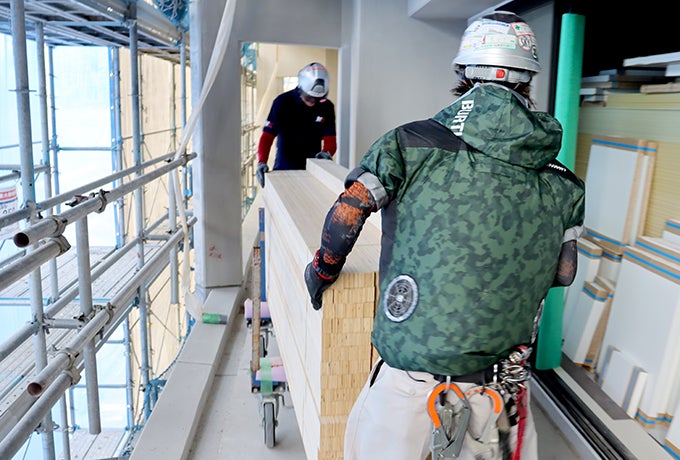 台車を使い、協力して長い資材を運ぶ2名の現場社員