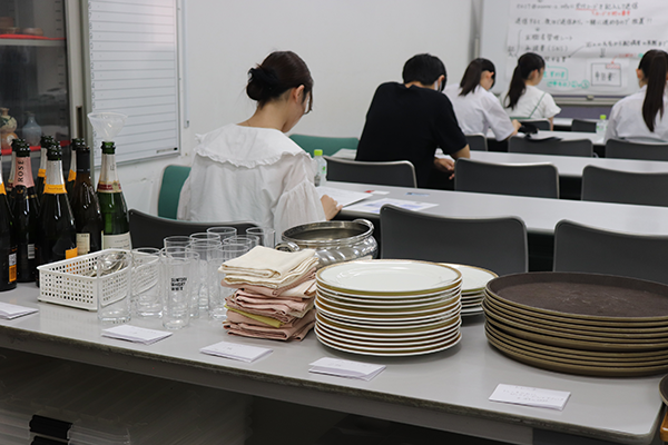 研修会場の後方に積まれた食器やお盆、クロス。講師がお手本を見せ、何回でも練習できる